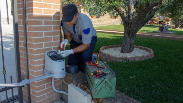 Technician working on an outdoor gate motor control box using tools and a multimeter for diagnostics.