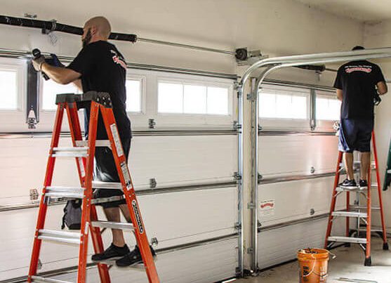 Technicians repairing garage door tracks and hardware using ladders inside a residential garage