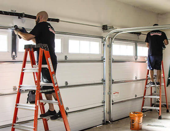 Technicians repairing garage door tracks and hardware using ladders inside a residential garage