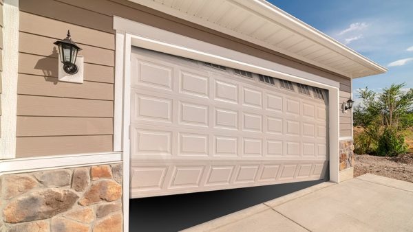 Beige sectional garage door on a suburban home exterior with stone accents and outdoor wall lanterns.